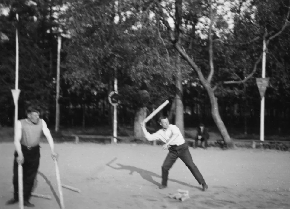 Чёрно-белая фотография: двое мужчин на площадке, один замахивается битой, другой стоит с битой